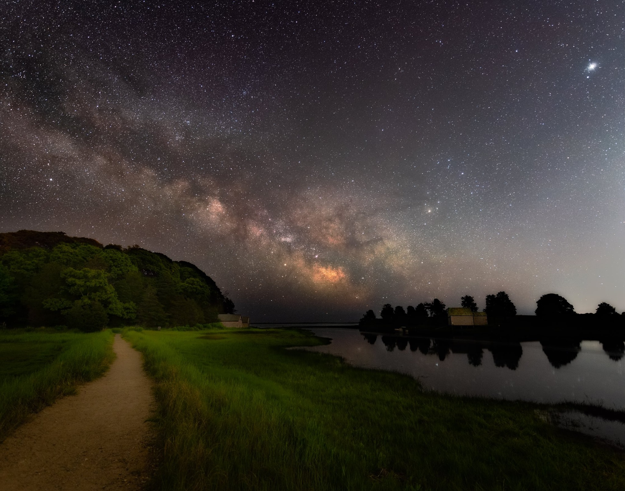 starlit night over the Nauset Marsh trail, adjacent to Salt Pond in Eastham. A trail winds through lush green grass, with a bright, starlit, Milky Way sky overhead.