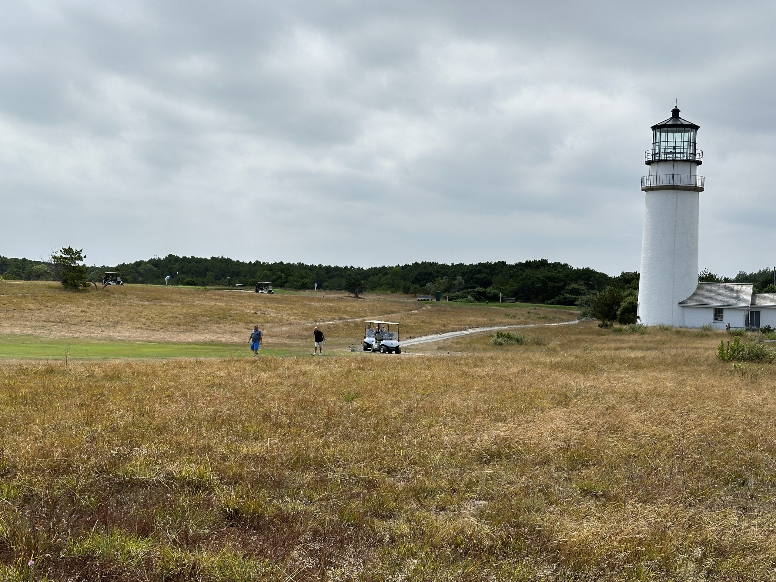 People playing golf adjacent to the Highland Lighthouse at Highland Links golf course.